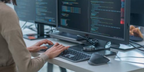 istockphoto-2085507701-612×612-1 close up hand of Asian prompt engineer developer coding app with software data sitting in front of computer monitor at office